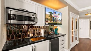 A modern kitchen with a stainless steel range hood, a coffee bar, and a flat-screen TV mounted above the counter.