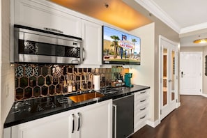 A modern kitchen with a stainless steel range hood, a coffee bar, and a flat-screen TV mounted above the counter.