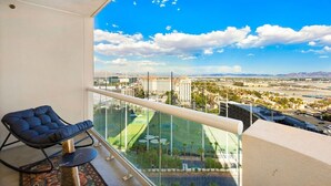 A balcony with a view of a cityscape, a lounge chair, and a pool area.