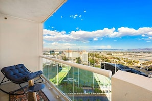 A balcony with a view of a cityscape, a lounge chair, and a pool area.