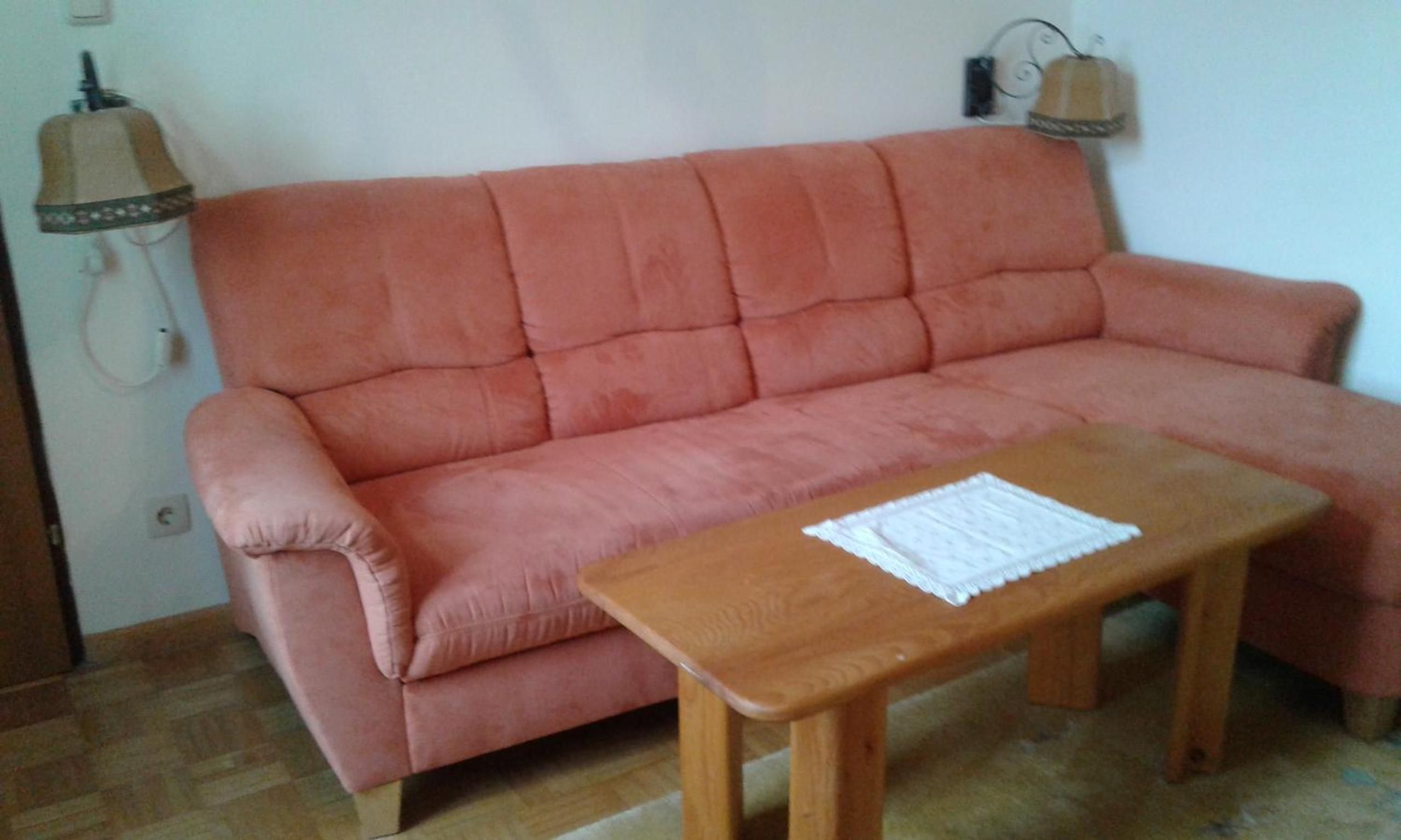 A pink sofa with a wooden coffee table in a room with a tiled floor.