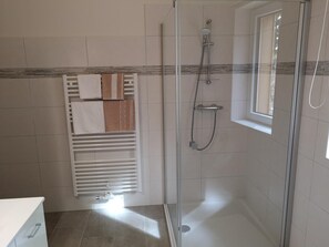 Douche met een glazen deur, een handdoekhouder met handdoeken, en een raam.