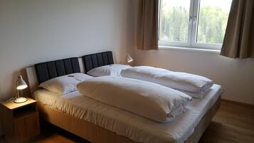 Ein Einzelbett mit Kopfteil, ein Nachttisch mit Lampe und ein Fenster mit Vorhängen.