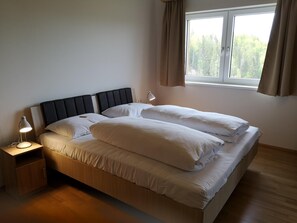 A single bed with a headboard, a bedside table with a lamp, and a window with curtains.