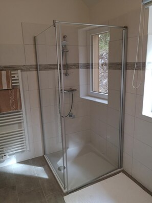 A glass-enclosed shower with a window, tiled walls, and a white floor.