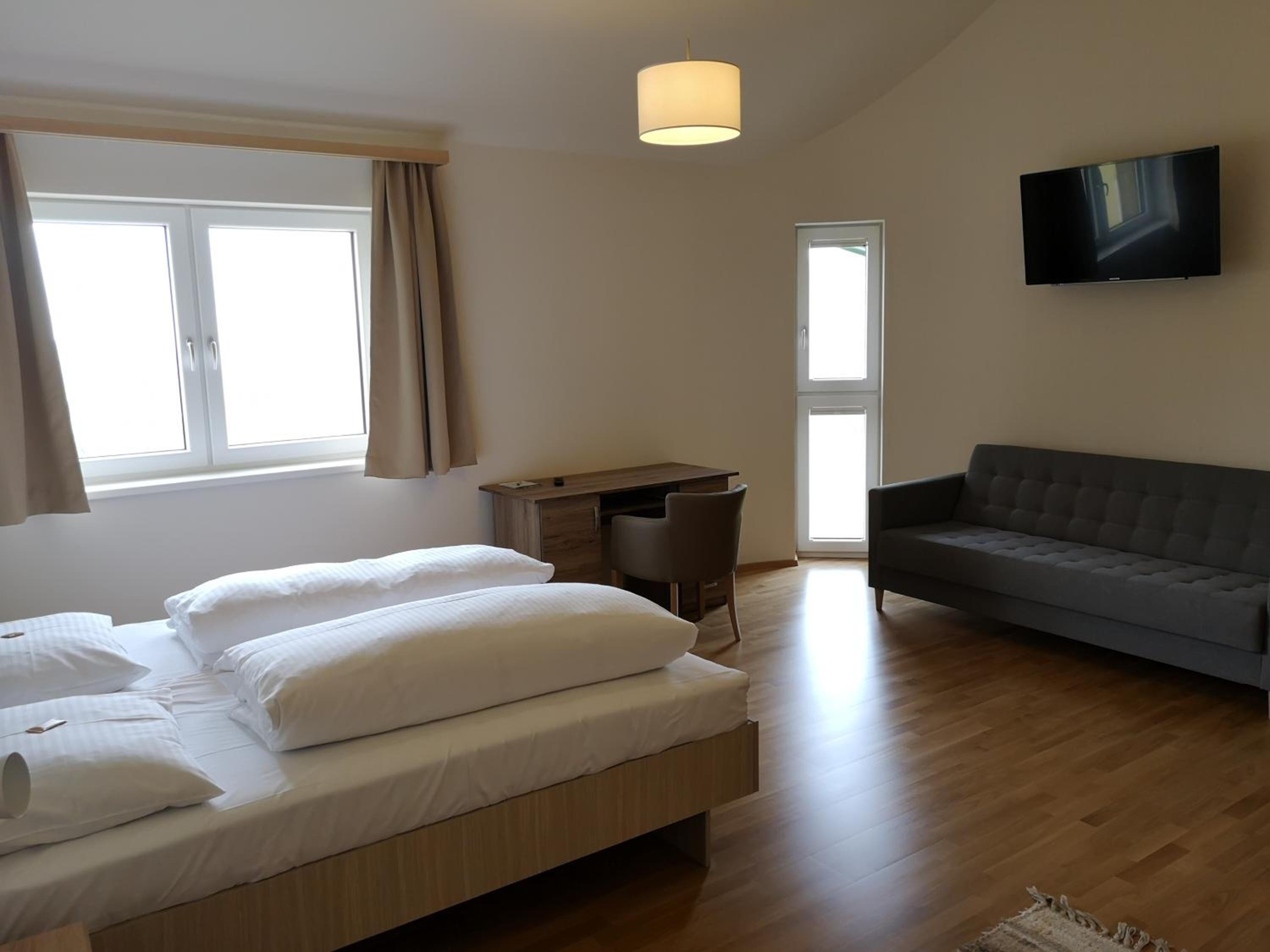 Ein modernes Hotelzimmer mit einem Bett, einem Schreibtisch, einem Sofa und einem Fernseher.
