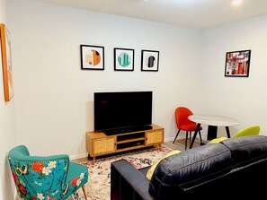 Una sala de estar con una televisión de pantalla plana, un sofá, una silla, una mesita y tres obras de arte enmarcadas en la pared.