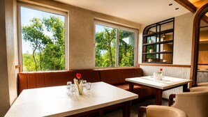 Un comedor con una mesa y sillas, ventanas amplias con vistas a árboles y un estante con vajilla.