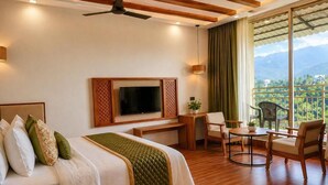Habitación de hotel con cama, televisión, escritorio, silla y balcón con vistas.