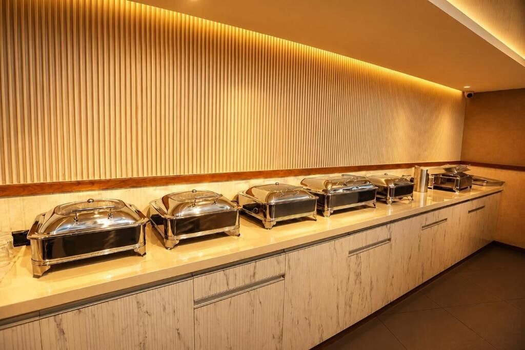 Mesa de buffet com recipientes de servir tampados e parede de painéis de madeira.
