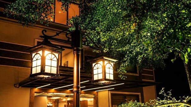 Un edificio con dos ventanas iluminadas de estilo farol y un árbol en primer plano.