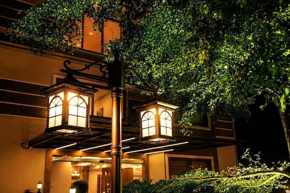 A building with two illuminated lantern-style windows and a tree in the foreground.