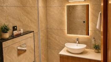 Un baño moderno con cabina de ducha de vidrio, inodoro blanco, lavabo con espejo y muebles de madera.