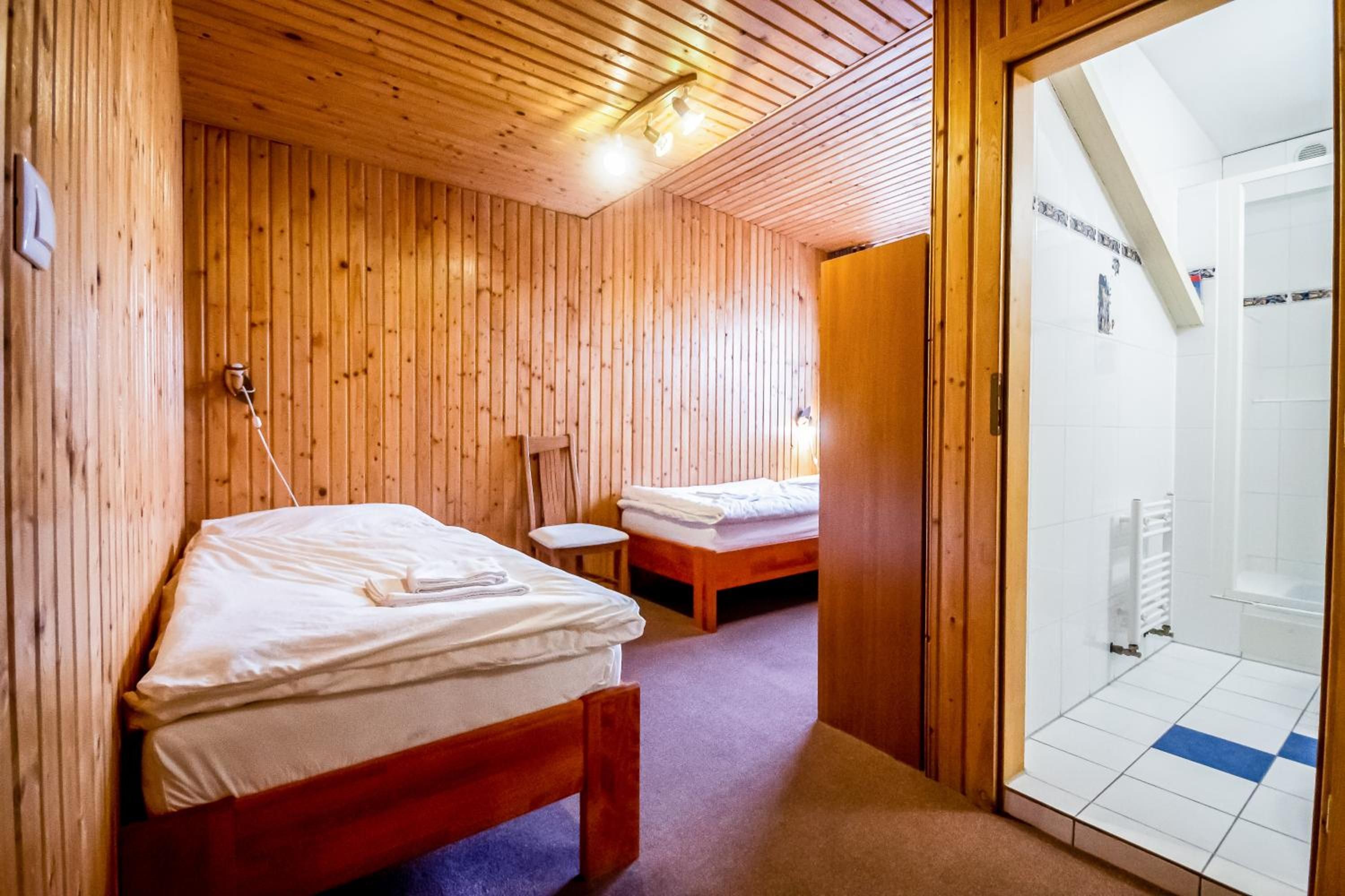 A wooden interior with two beds, a small table, and a shower area.