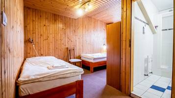 A wooden interior with two beds, a small table, and a shower area.