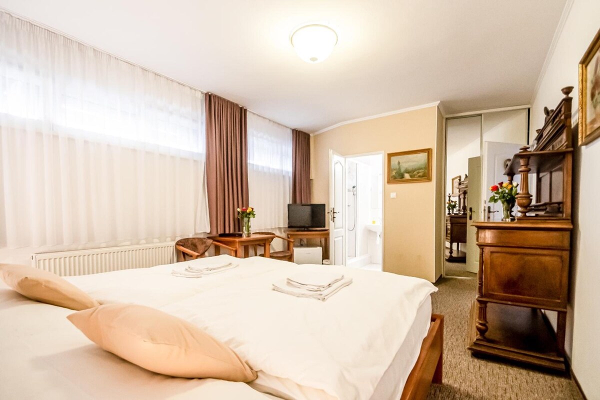 A hotel room with a bed, a desk, a television, and a bathroom visible through an open door.