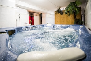 A hot tub with a wooden wall and a potted plant in the background.