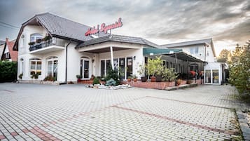 Un hotel con techo de tejas, un letrero que dice 'Hotel Squash' y un área de acceso pavimentada con plantas en macetas.