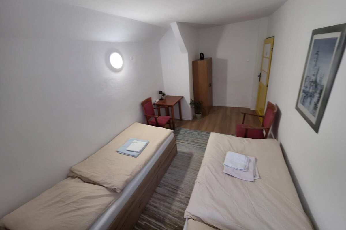 A small, single-room accommodation with two single beds, a desk, a chair, and a wardrobe.