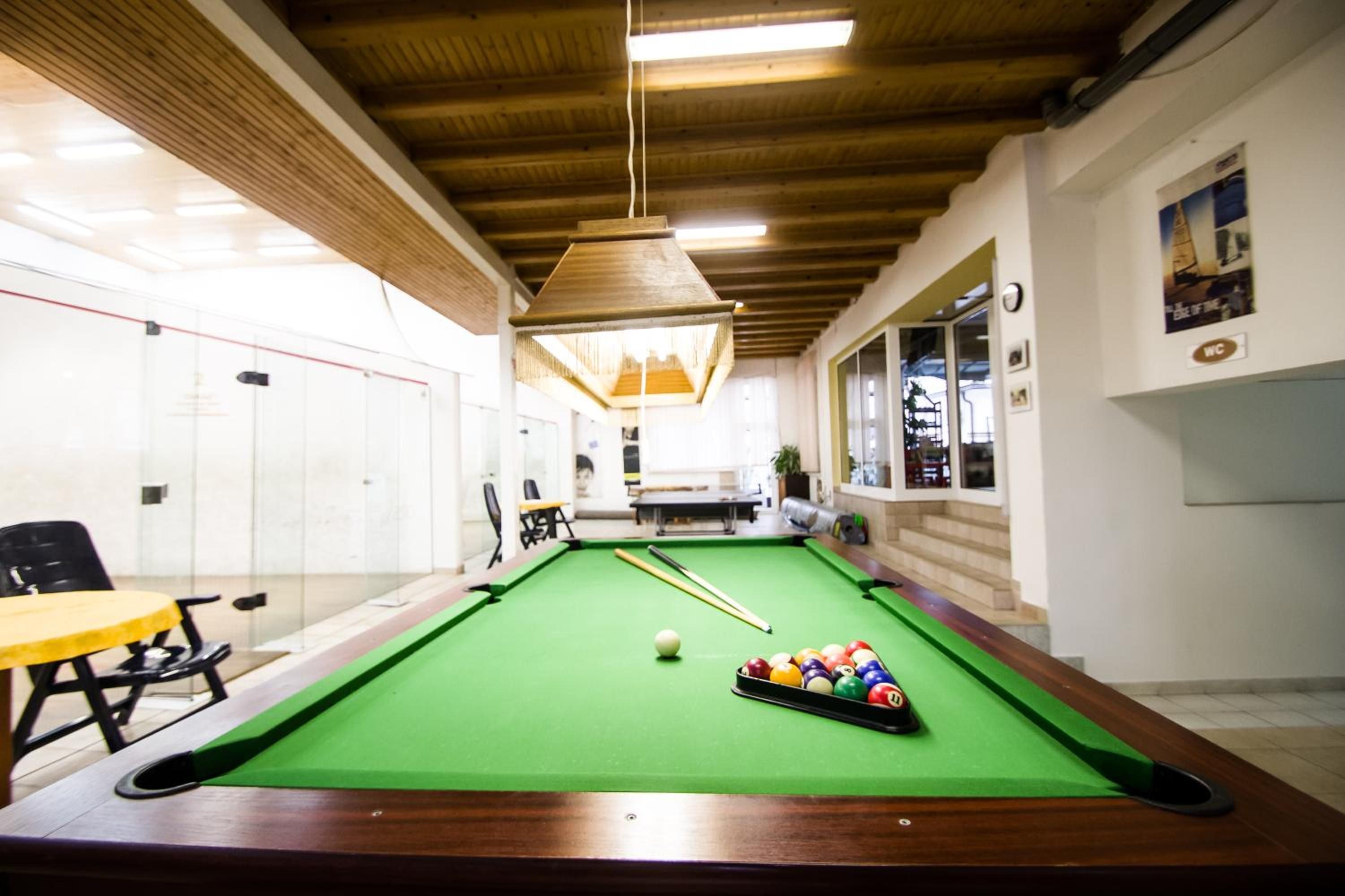 A pool table with balls, a yellow table, and chairs in a room with wooden ceilings and white walls.