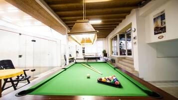 A pool table with balls, a yellow table, and chairs in a room with wooden ceilings and white walls.