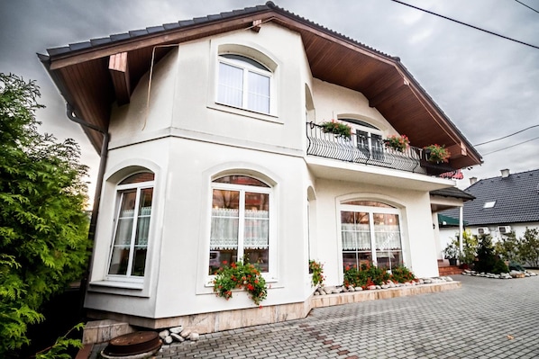 A two-story building with a balcony on the upper floor, large windows, and a stone foundation.