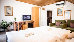 Habitación de hotel con una cama, un escritorio con computadora, un sofá verde y obras de arte en las paredes.