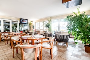 A hotel lobby with multiple seating areas, including round tables and sofas, and a large potted plant.