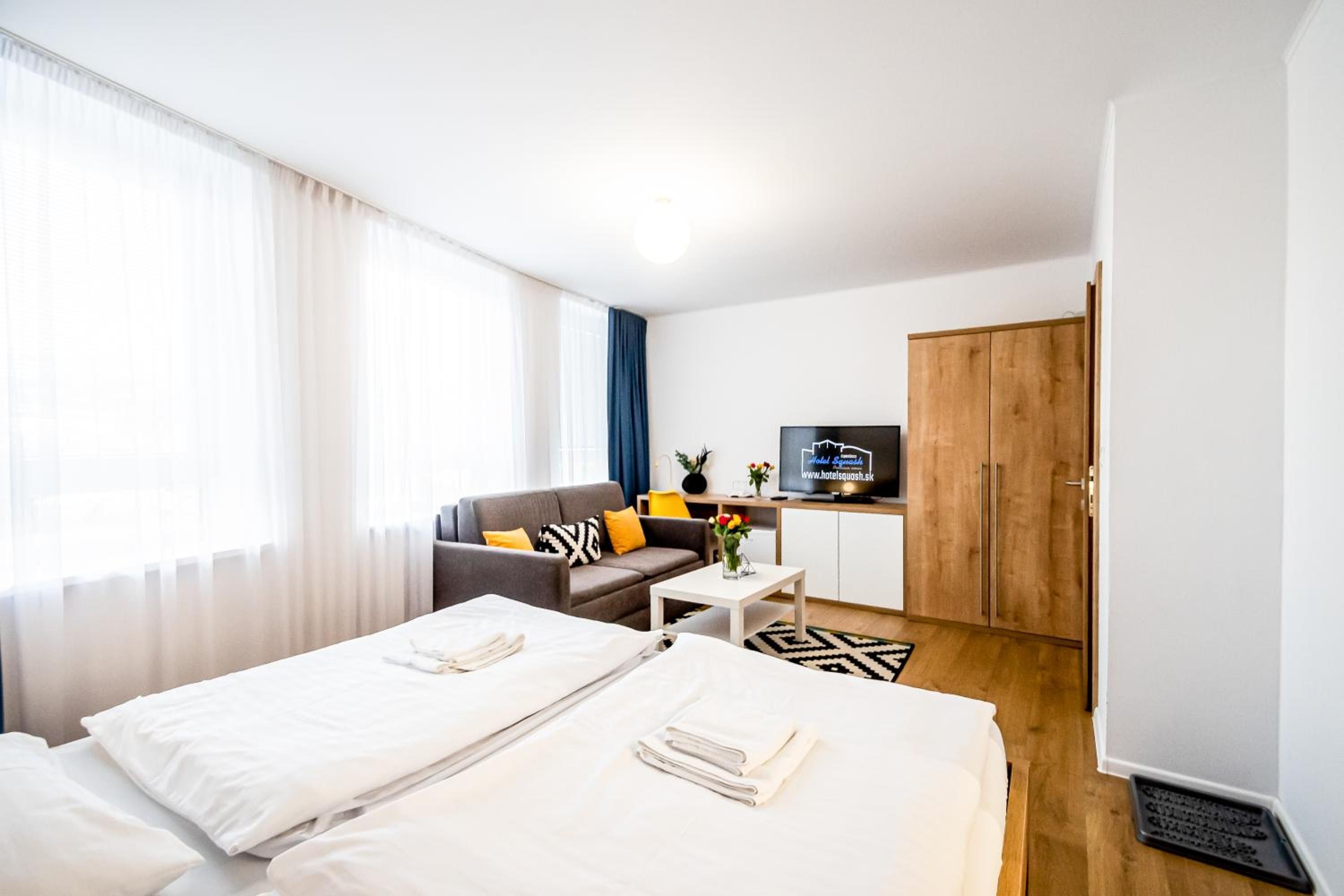 A hotel room with two beds, a sofa, a small table, a TV, and a wardrobe.
