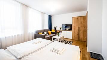 A hotel room with two beds, a sofa, a small table, a TV, and a wardrobe.
