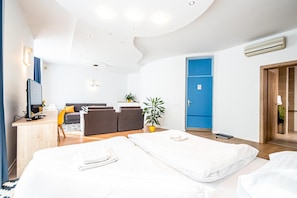 Ein modernes Hotelzimmer mit einem Bett, einem Schreibtisch mit Computer, einer Couch und einer blauen Tür.