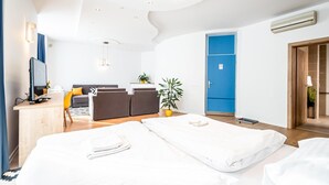 Una habitación de hotel moderna con cama, escritorio con computadora, sofá y una puerta azul.