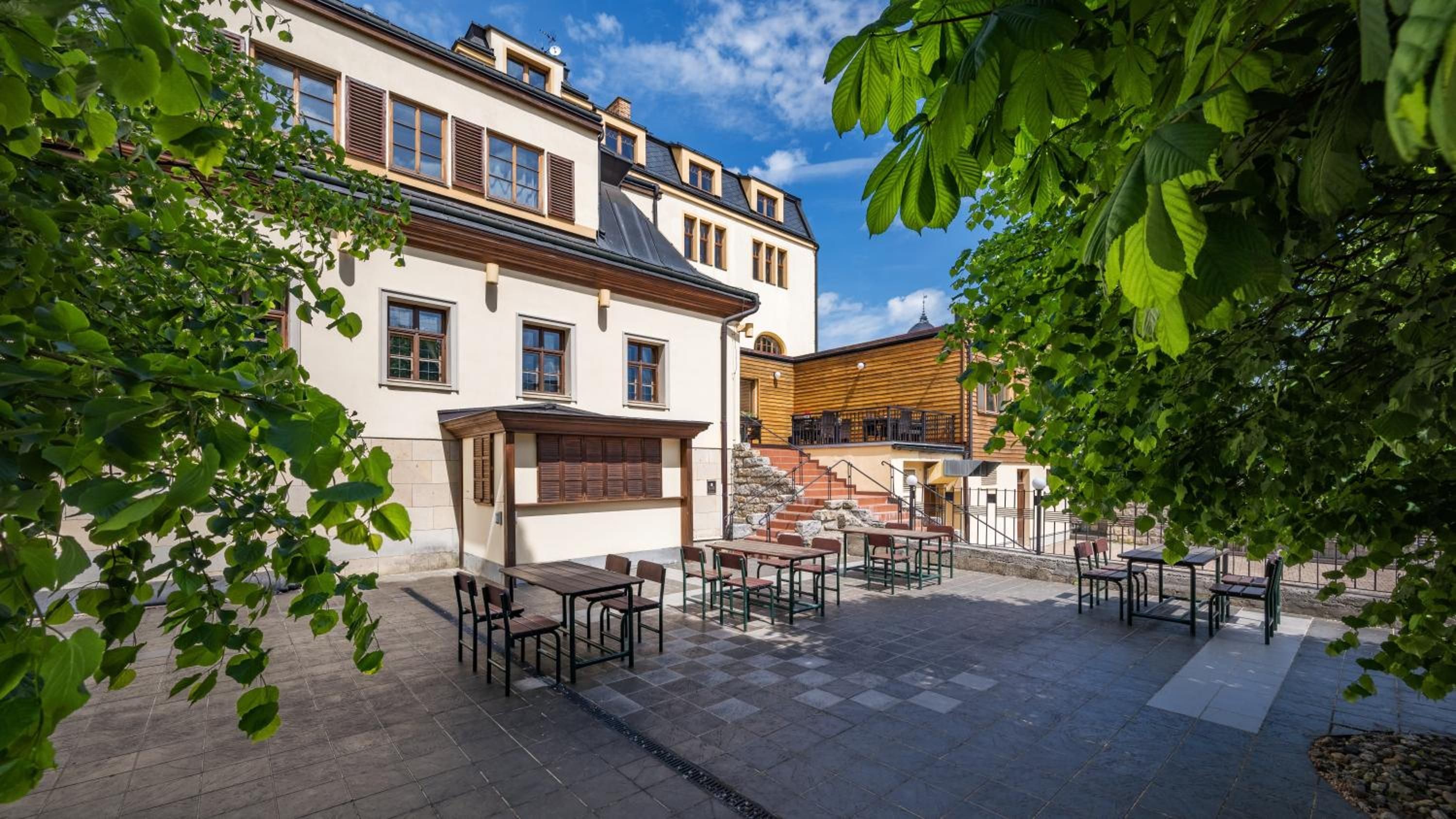 Un patio con mobiliario exterior, una escalera y un edificio con múltiples ventanas y fachada de madera.