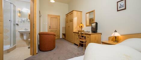 A hotel room with a bed, desk, chair, and a small stool.