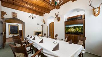 A dining room with a long table set for a meal, wooden chairs, a chandelier, and mounted animal heads on the walls.