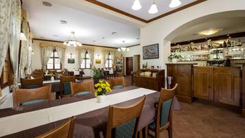 A dining area with a long table, chairs, and a bar area with shelves of bottles.