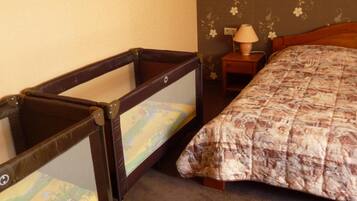 A room with a bed, a small table with a lamp, and a baby crib.