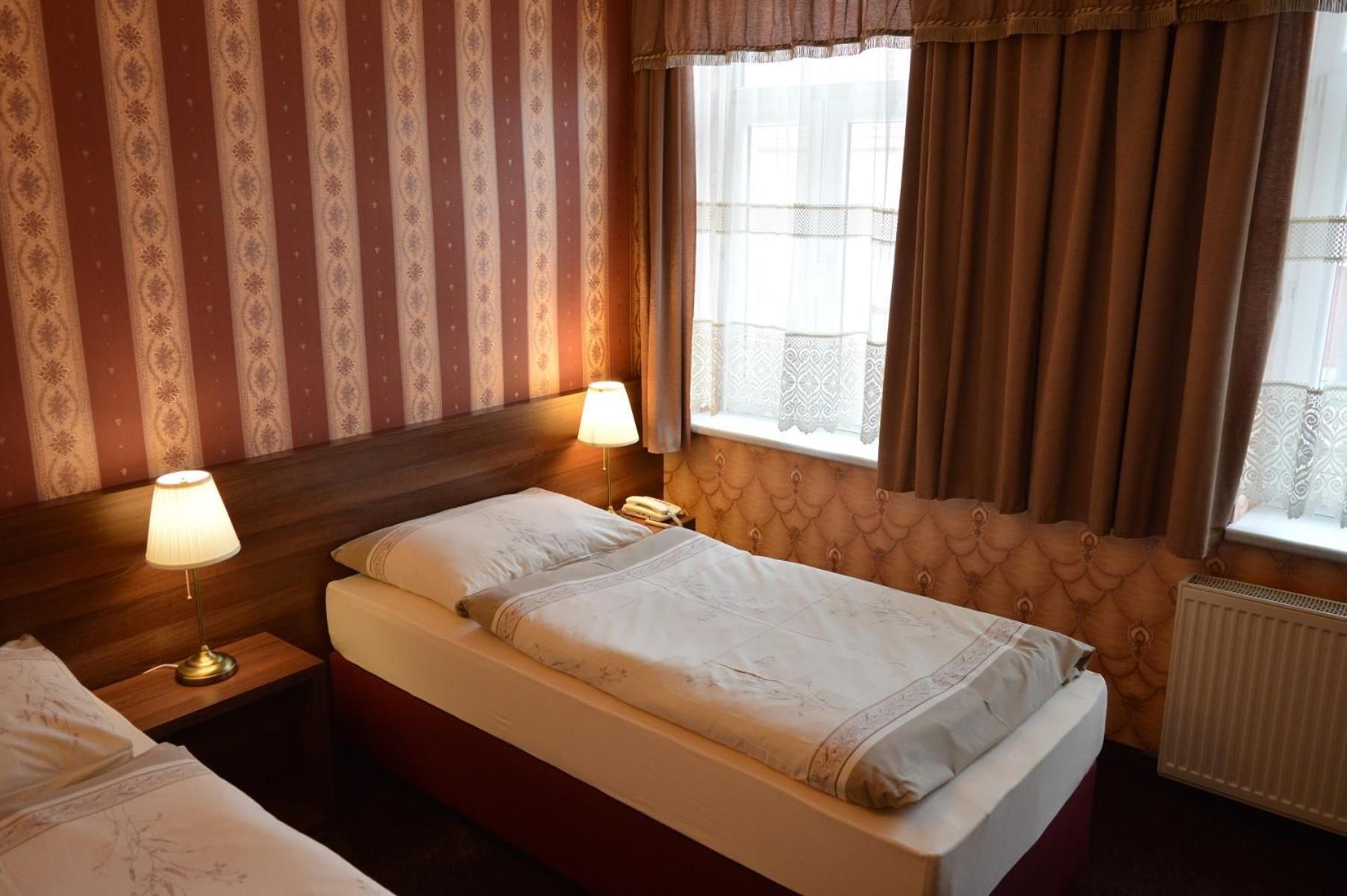 A hotel room with a single bed, a bedside table with a lamp, and a window with curtains.