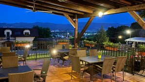 Un patio exterior con mesas y sillas, vistas de la ciudad y montañas al fondo.