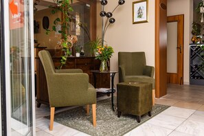 Une pièce comprenant deux fauteuils, une petite table, un vase avec des fleurs et un meuble à bouteilles.