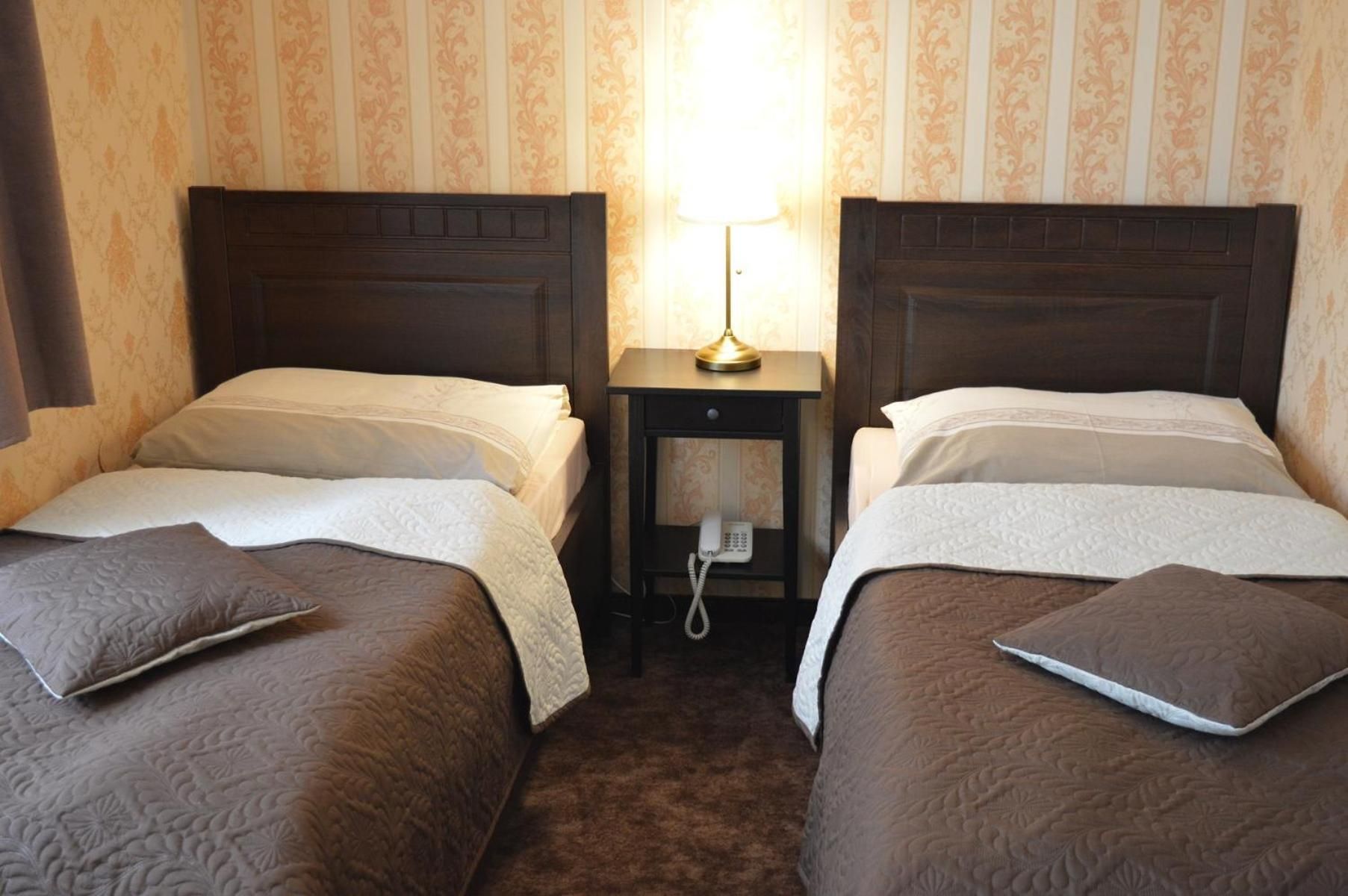 A hotel room with two single beds, a bedside table with a lamp, and a telephone.