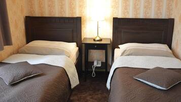 A hotel room with two single beds, a bedside table with a lamp, and a telephone.