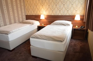 A hotel room with two single beds, a wooden headboard, a telephone, and a lamp on each nightstand.