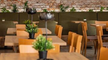 A restaurant interior with brick walls, a neon sign, wooden tables, and green plants.