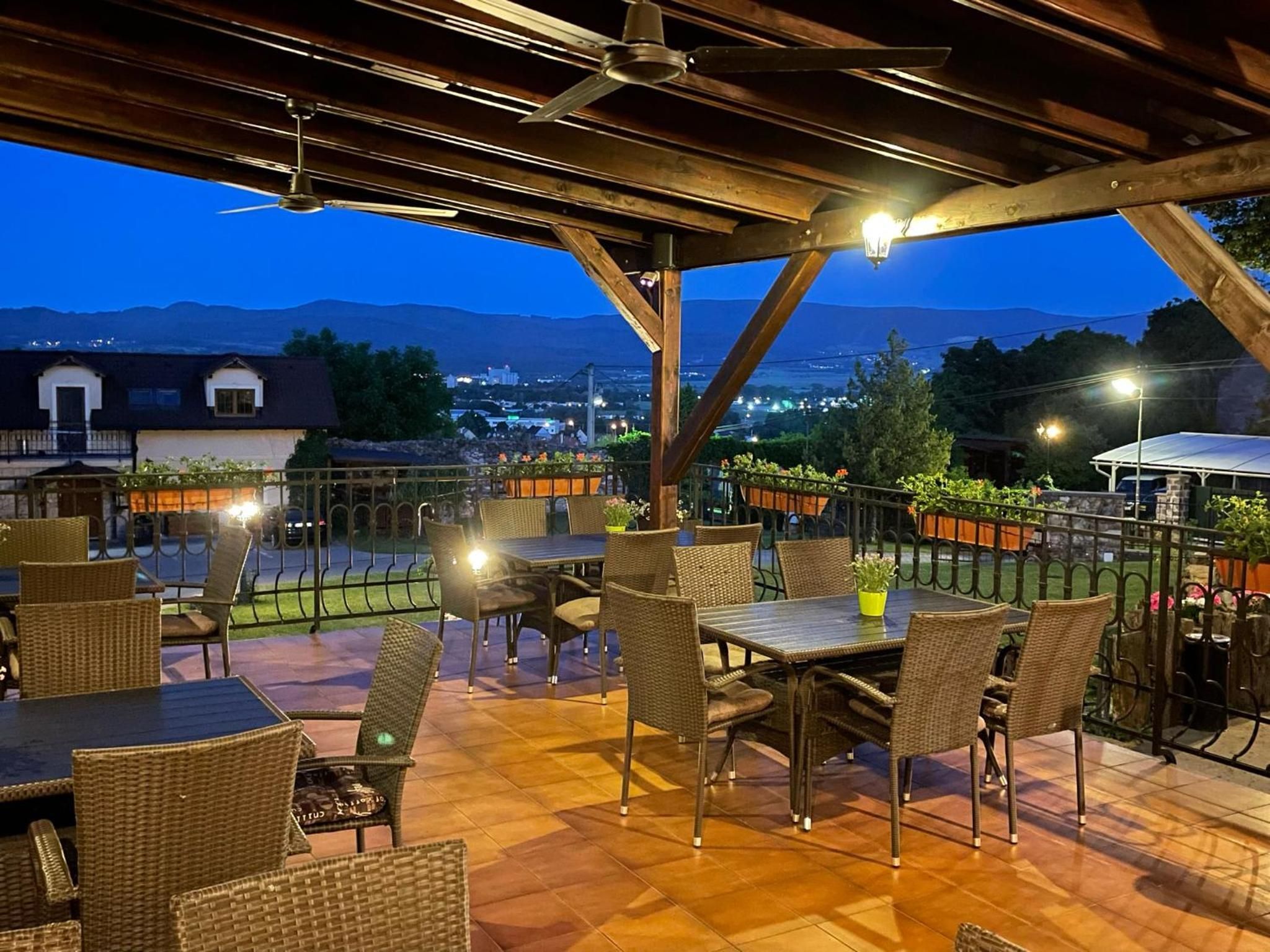 Un patio exterior con mesas y sillas, vistas de la ciudad y montañas al fondo.