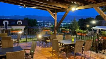 Un patio exterior con mesas y sillas, vistas de la ciudad y montañas al fondo.
