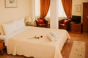 Ein Hotelzimmer mit einem großen Bett, zwei Stühlen, einem Fernseher und einem kleinen Schrank.