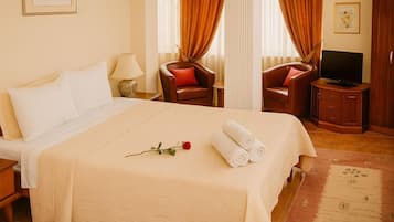 A hotel room with a large bed, two chairs, a television, and a small cabinet.