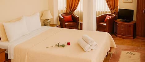 A hotel room with a large bed, two chairs, a television, and a small cabinet.