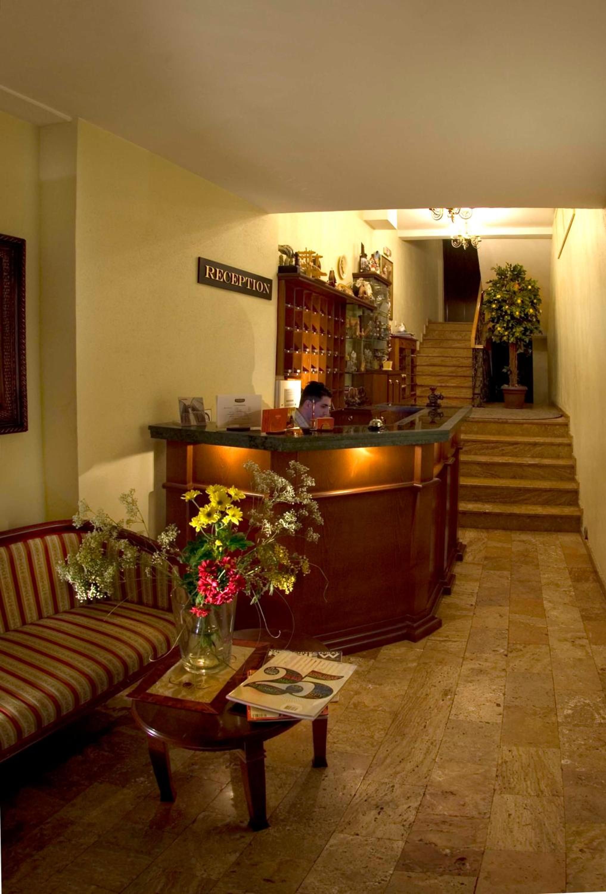 A reception area with a reception desk, a sofa, a vase with flowers, and a staircase leading upstairs.